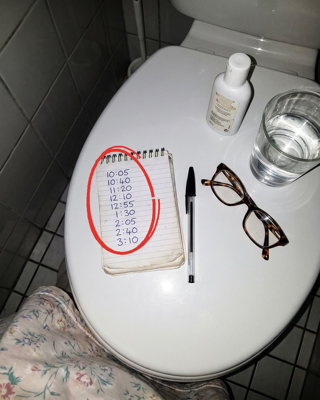 A notepad on a closed toilet lid listing nine times in one night, circled in red, with reading glasses and a glass of water