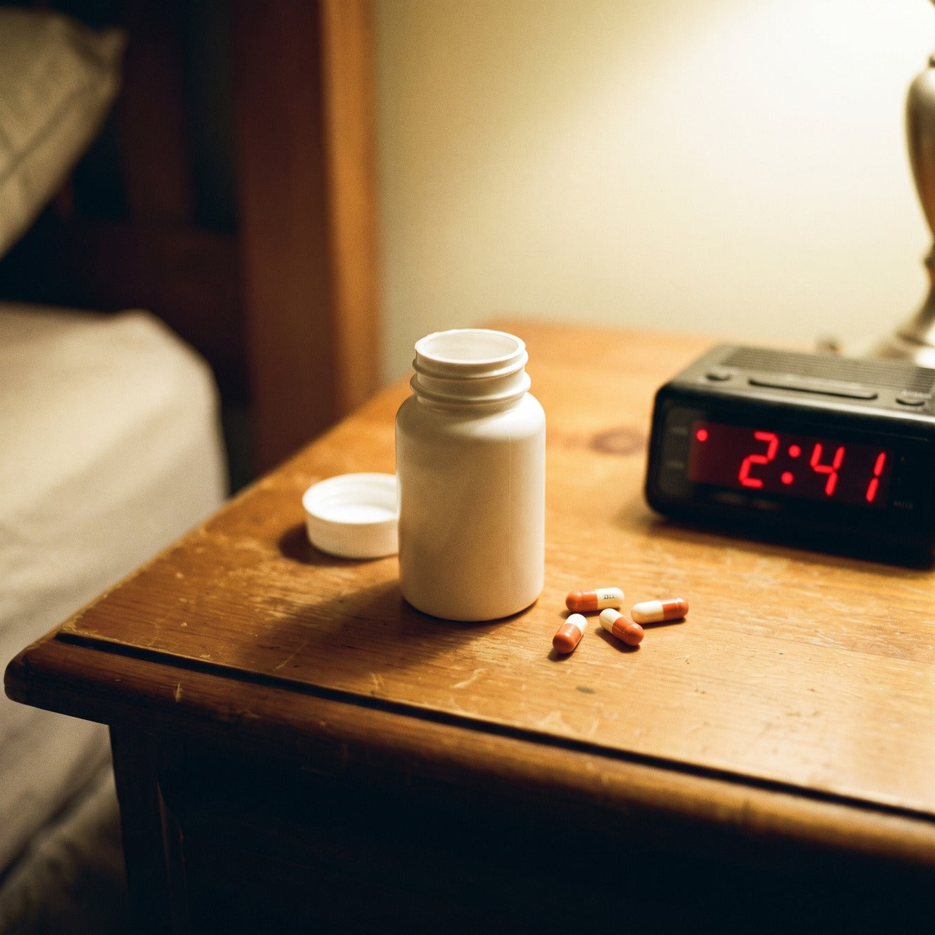 A bottle of pills open on a nightstand next to an alarm clock