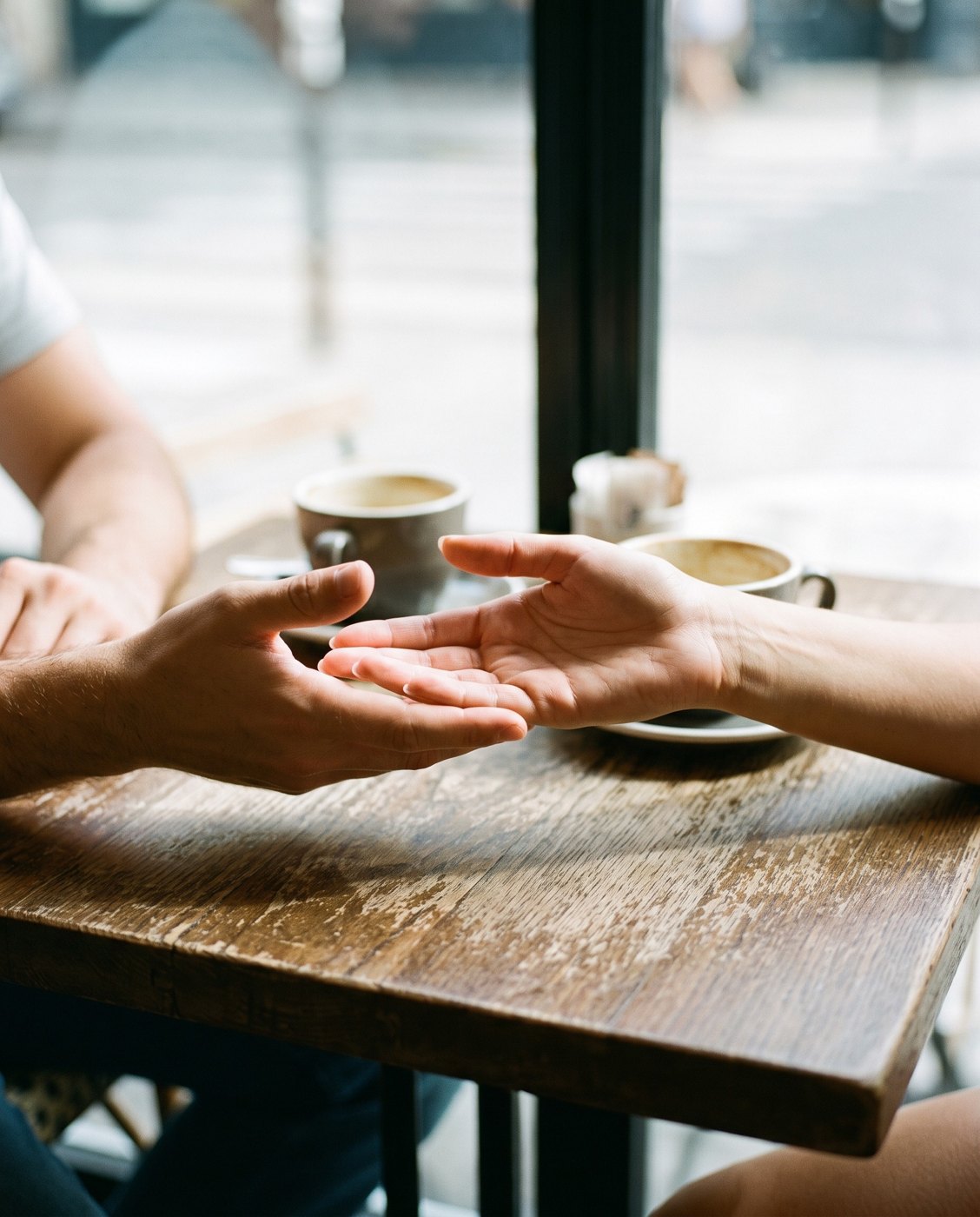 A hand held out to shake another across a cafe table