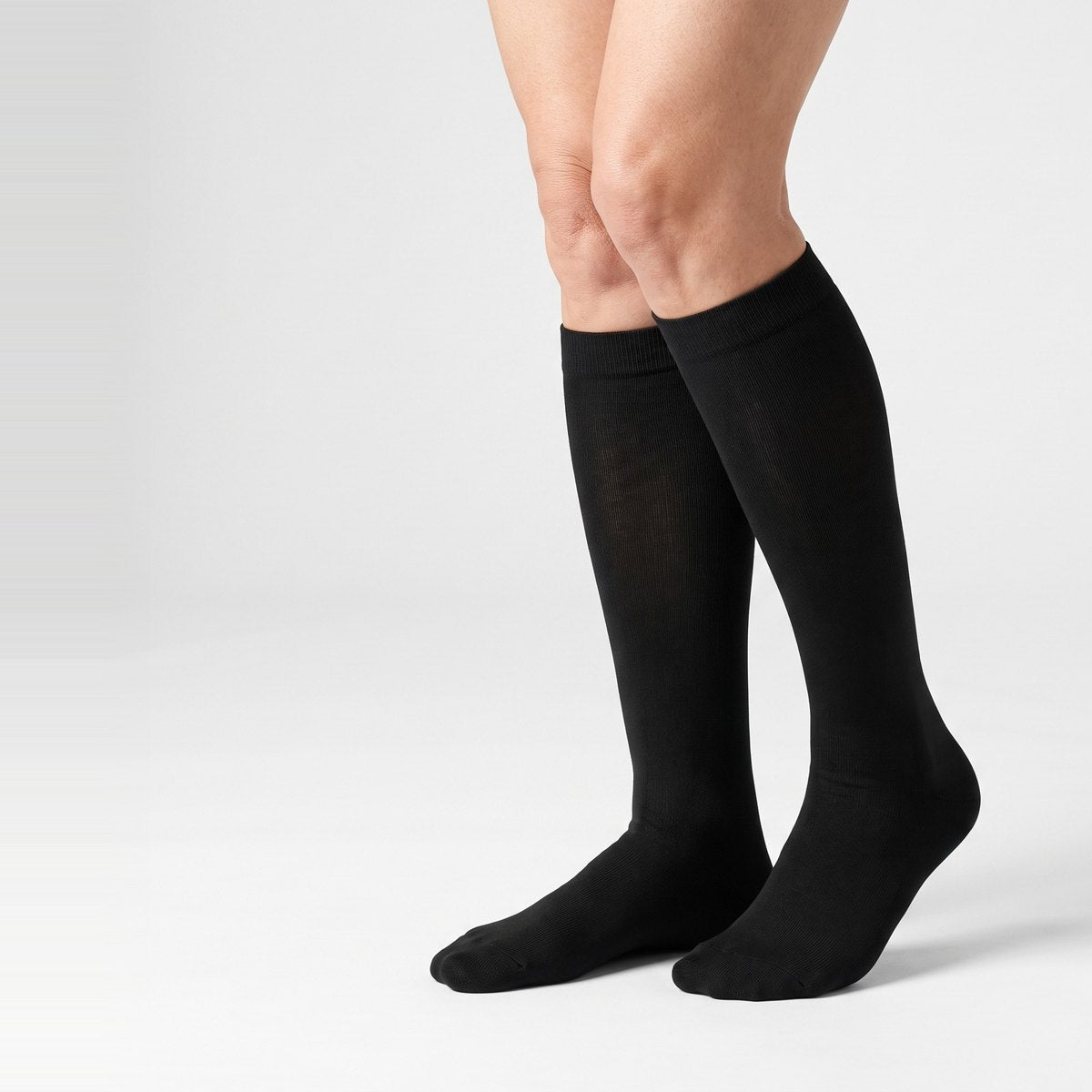 A woman's legs in plain black knee-high compression socks against a white background